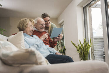 Happy senior couple and home caregiver using tablet PC in living room - UUF31212