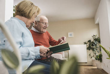 Lächelnde ältere Frau und Mann betrachten Fotos in einem Album zu Hause - UUF31216