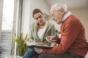 Home caregiver with senior man looking at photo album - UUF31217