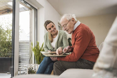 Smiling home caregiver with man holding photo album - UUF31218