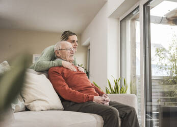 Lächelnde Hauspflegerin mit älterem Mann auf dem Sofa sitzend - UUF31224