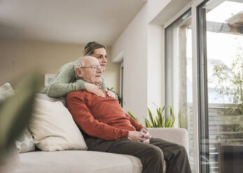 Smiling home caregiver with senior man sitting on sofa - UUF31224