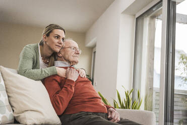 Lächelnde häusliche Pflegerin umarmt älteren Mann auf dem Sofa sitzend - UUF31225