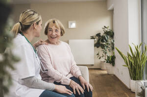 Glücklicher Arzt, der sich um eine ältere Frau zu Hause kümmert und ihr Ratschläge gibt - UUF31228