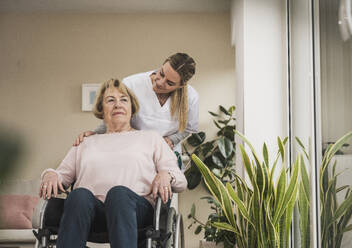 Hauspflegerin mit einer älteren Frau, die zu Hause im Rollstuhl sitzt - UUF31241