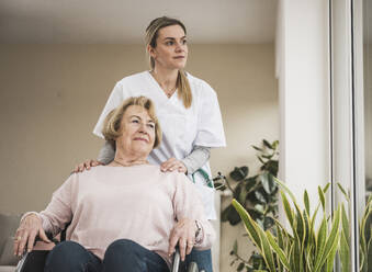 Nurse with senior woman sitting in wheelchair at home - UUF31242