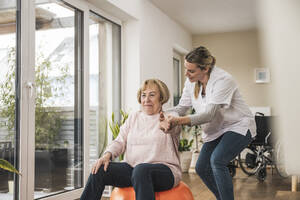 Krankenschwester mit einer älteren Frau, die zu Hause Übungen macht - UUF31246