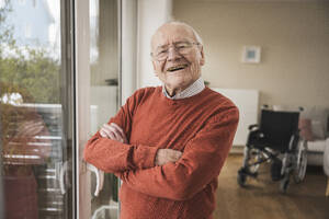 Glücklicher älterer Mann, der mit verschränkten Armen zu Hause steht - UUF31253