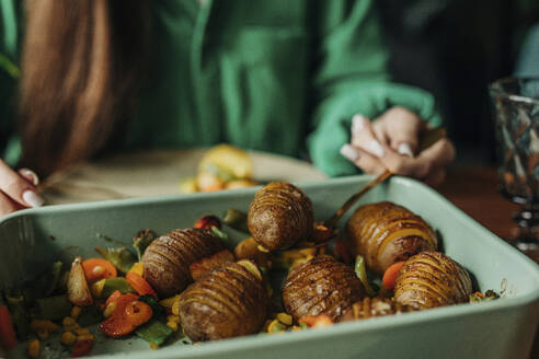 Woman picking up freshly baked potatoes from casserole dish at Easter dinner - VSNF01655