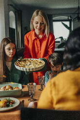 Lächelnde Frau serviert der Familie beim Osteressen herzhaften Kuchen - VSNF01657