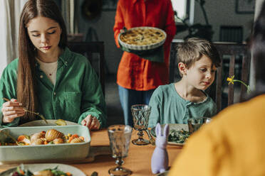 Geschwister essen eine Mahlzeit am Esstisch beim Osterfestessen - VSNF01658