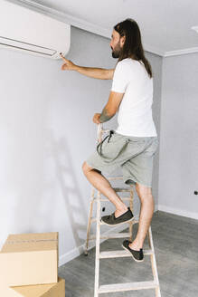 Mann steht auf einer Leiter und schaltet die Klimaanlage in seinem neuen Haus ein - DAMF01307