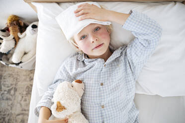 Sick boy lying down on bed with compress over forehead at home - NJAF00767
