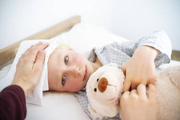 Mother taking care of sick son lying down with teddy bear on bed at home - NJAF00768