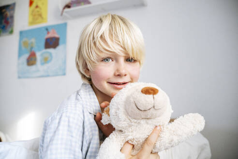 Smiling blond boy with teddy bear at home - NJAF00773