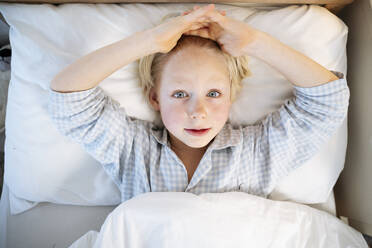 Boy with head in hands lying down on bed at home - NJAF00782