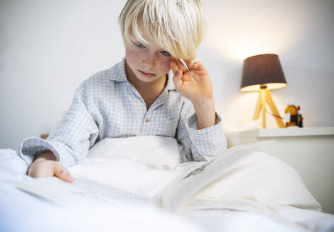 Boy reading book in bedroom at home - NJAF00786