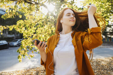 Beautiful redhead woman listening to music in autumn - ALKF00964