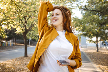 Smiling woman with head in hand day dreaming at autumn park - ALKF00966