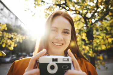 Lächelnde Frau hält Kamera an einem sonnigen Tag im Herbst - ALKF00967