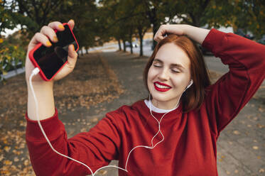 Happy woman listening to music with eyes closed in autumn - ALKF00981