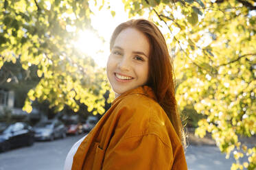 Lächelnde Frau an einem sonnigen Tag in der Nähe eines Baumes im Herbst - ALKF00982