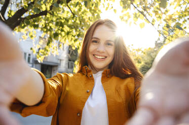 Glückliche Frau nimmt Selfie in der Nähe von Baum an sonnigen Tag - ALKF00983