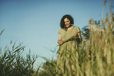 Smiling woman standing in field on sunny day - IEF00542