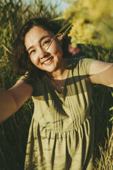 Lächelnde reife Frau nimmt Selfie inmitten von Gras im Feld - IEF00549