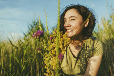 Glückliche Frau mit einem Strauß Wildblumen auf einem Feld an einem sonnigen Tag - IEF00550