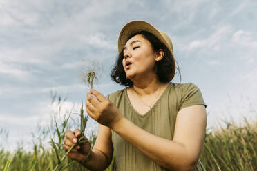 Playful woman blowing on dandelion in field - IEF00565