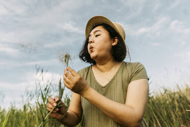 Carefree mature woman blowing on dandelion in field - IEF00566