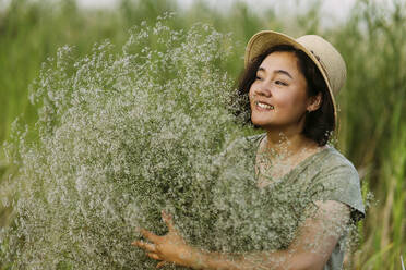 Smiling woman holding bunch of gypsophila flowers in field - IEF00570