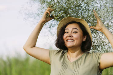 Happy mature woman carrying gypsophila flowers on head in field - IEF00572