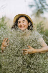 Happy woman holding bunch of gypsophila flowers in field - IEF00579