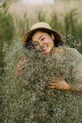Lächelnde Frau, die einen Strauß Schleierkrautblüten auf einem Feld umarmt - IEF00582