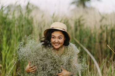 Cheerful woman holding bunch of gypsophila flowers in field - IEF00587