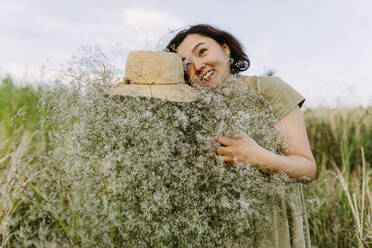 Unbekümmerte Frau umarmt einen Strauß Schleierkrautblüten auf einem Feld - IEF00592