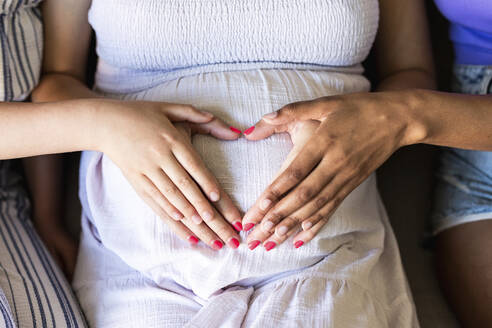 Familie macht Herzzeichen mit Händen auf dem Bauch der schwangeren Frau zu Hause - WPEF08407