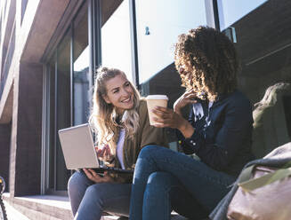 Happy business colleagues sitting and talking near building - UUF31266