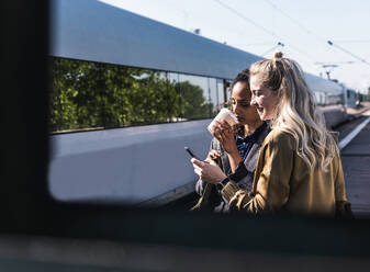 Businesswoman sharing smart phone with coworker at station platform - UUF31269