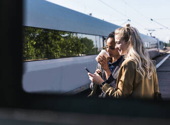 Geschäftsfrau teilt ihr Smartphone mit einem Kollegen am Bahnsteig - UUF31269