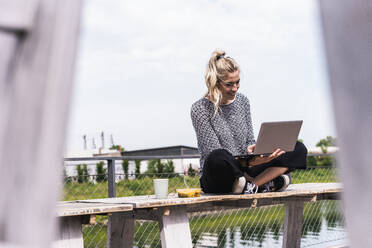 Young businesswoman sitting on bench and using laptop - UUF31283