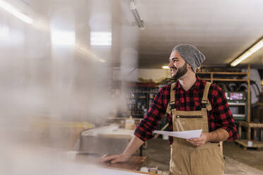 Lächelnder Schreiner mit Dokument in der Werkstatt - UUF31296