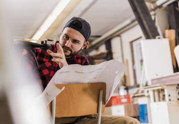 Konzentrierter Handwerker, der eine auf einem Stuhl sitzende Drohne in der Werkstatt untersucht - UUF31309