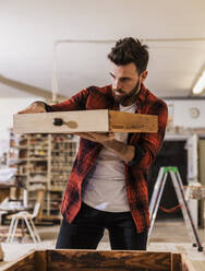 Tischler, der in der Werkstatt stehend eine Holzschublade untersucht - UUF31319