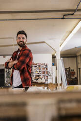 Smiling carpenter standing with arms crossed at workshop - UUF31322