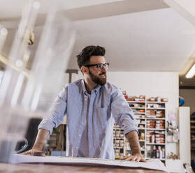 Smiling craftsman leaning on table at workshop - UUF31325