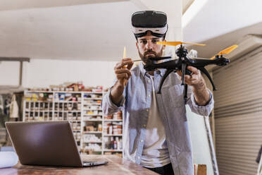 Engineer wearing VR glasses and examining drone at workshop - UUF31326