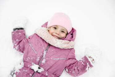 Playful girl wearing winter jacket and lying on snow - EYAF02952